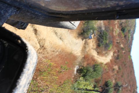 1992 Ford Bronco - The photo shows a view from inside a vehicle, looking out over a dry, hilly landscape with a dirt road winding through it.