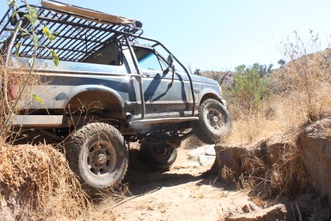1992 Ford Bronco - This modified Ford Bronco is navigating a challenging off-road trail with steep inclines and rocky terrain.