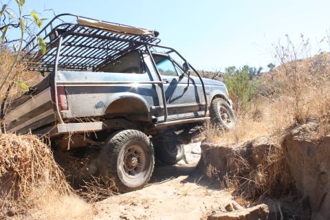 1992 Ford Bronco - A blue 1992 Ford Bronco navigates a challenging off-road trail with steep inclines and dry brush.