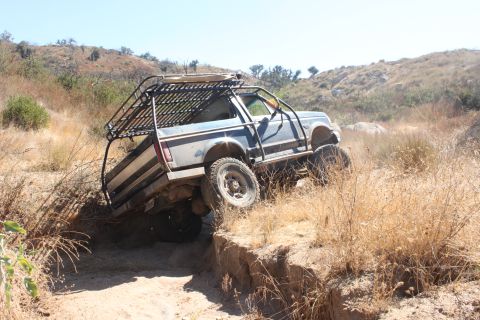 1992 Ford Bronco - Modified blue truck with a custom roof rack navigates a challenging off-road trail.