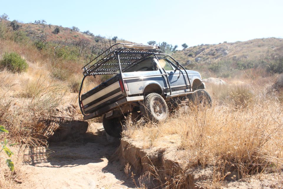 1992 Ford Bronco with roll cage and roof rack navigating a steep dirt ditch