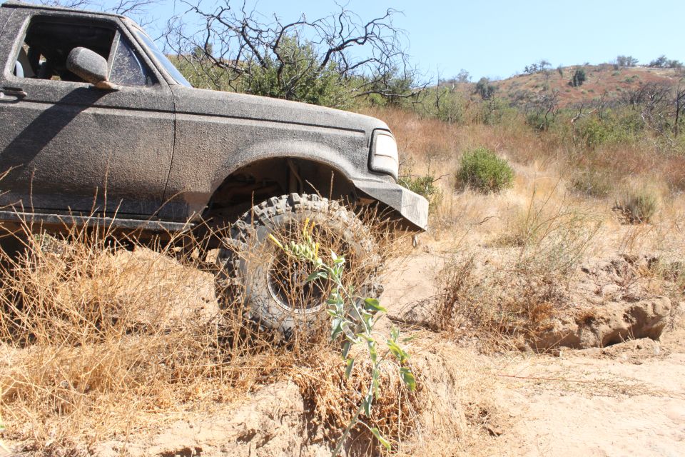 Mud-caked SUV driving off-road, front wheel visible, dry brush and hills in background