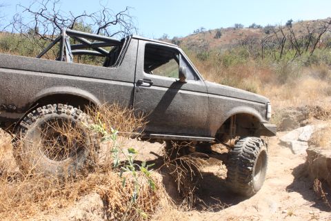 1992 Ford Bronco - This heavily modified SUV navigates a rough, dry terrain with large off-road tires.
