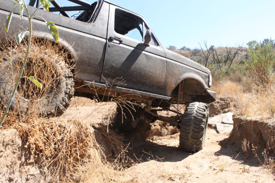 Modified 1992 Ford Bronco climbing over rough terrain on a dry, sunny day