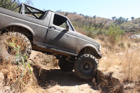 1992 Ford Bronco - A 1992 Ford Bronco navigates a challenging off-road trail with steep inclines and dry vegetation.