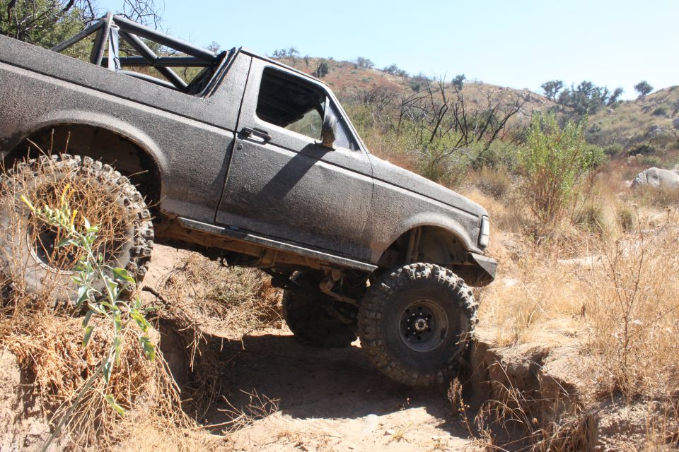 Dark gray 1992 Ford Bronco off-roading on a dirt trail, with large tires and a roll cage