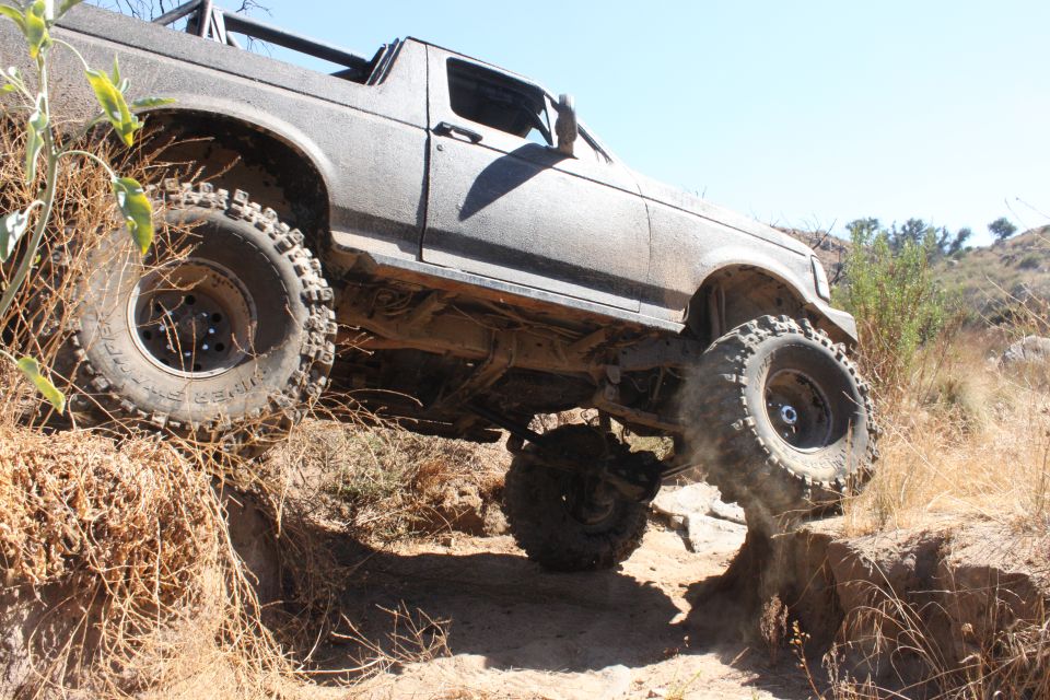 1992 Ford Bronco climbing over rocks on a dirt trail, front passenger side wheel elevated