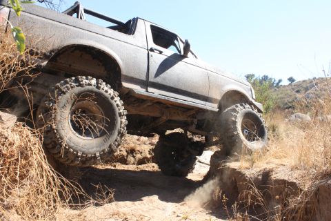 1992 Ford Bronco - A 1992 Ford Bronco tackles a challenging off-road trail with large tires and a lifted suspension.