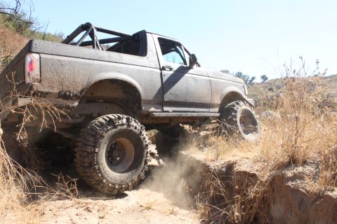 1992 Ford Bronco - This modified 1992 Ford Bronco navigates a steep, dusty trail with large off-road tires.