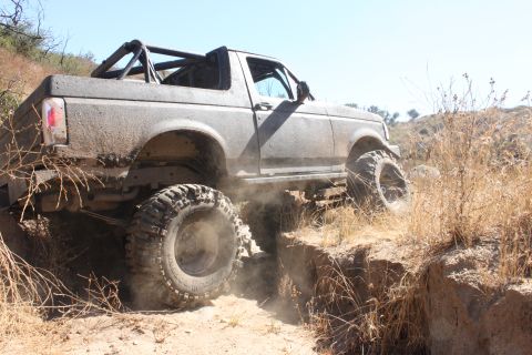 1992 Ford Bronco - This heavily modified truck navigates a challenging off-road obstacle on a sunny day.