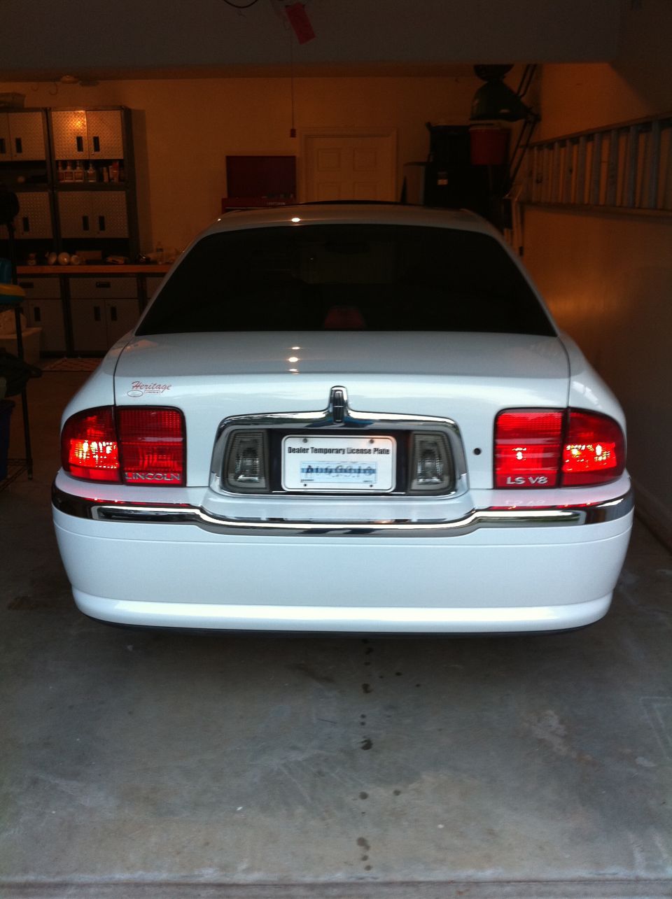 Rear of white Lincoln LS V8 sedan in garage with lit taillights and temporary dealer plate