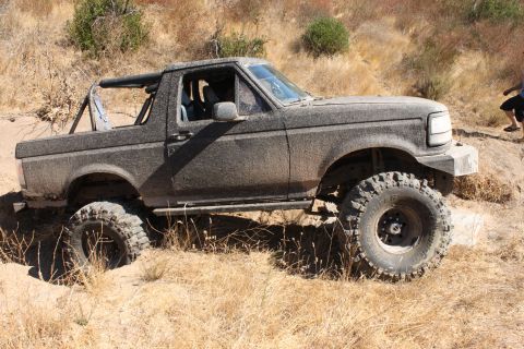 1992 Ford Bronco - A heavily modified 1992 Ford Bronco navigates a dirt trail with large, aggressive tires.