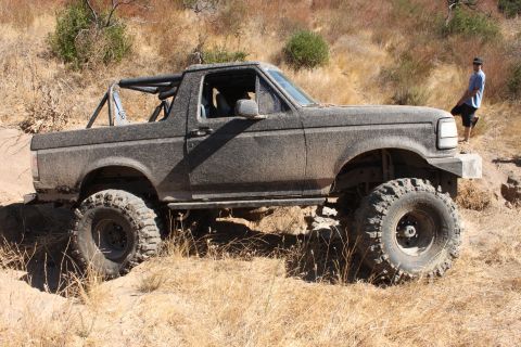 1992 Ford Bronco - Modified 1992 Ford Bronco navigating a rough, dry terrain with large tires and a roll cage.
