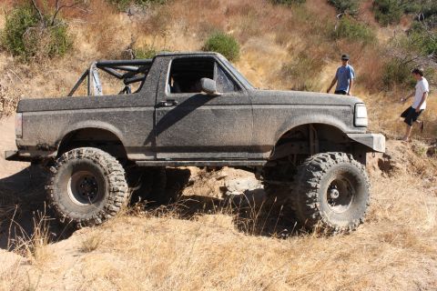 1992 Ford Bronco - A heavily modified 1992 Ford Bronco navigates a dry, grassy trail with two people observing.