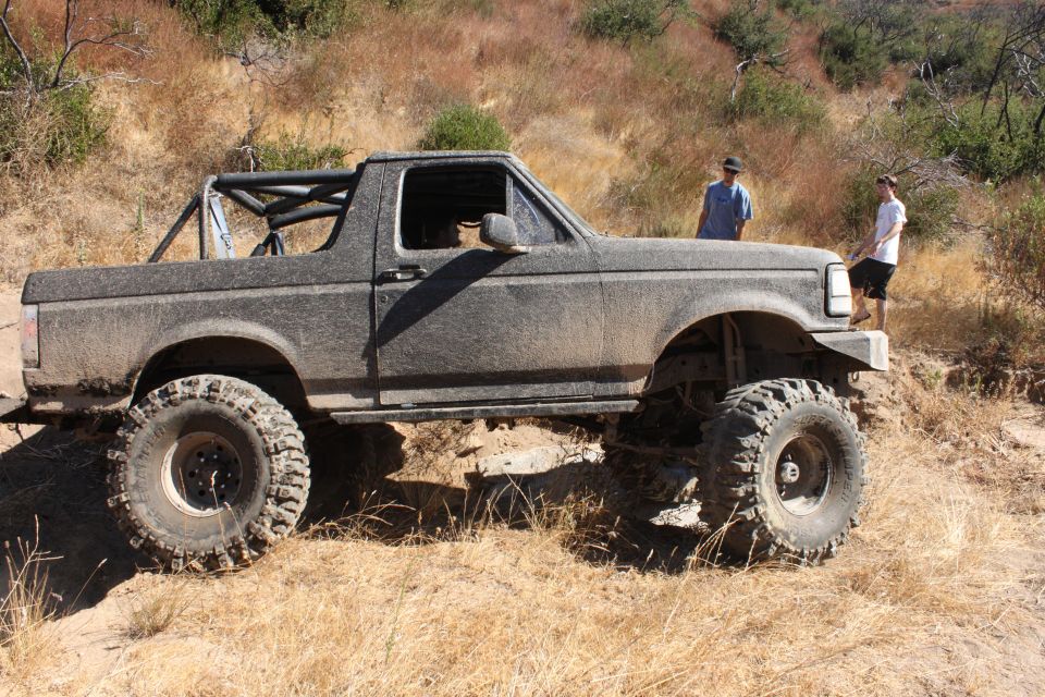 Side view of a lifted 1992 Ford Bronco covered in mud, with off-road tires on a dirt trail