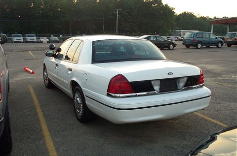 2001 Ford Crown Victoria - A white 2001 Ford Crown Victoria sedan is parked in an outdoor lot with other vehicles visible.