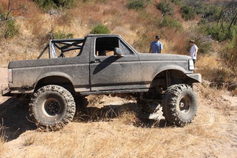 1992 Ford Bronco - A heavily modified Ford Bronco sits on a dry, grassy hillside with two people standing nearby.