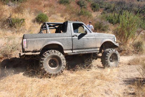 1992 Ford Bronco - A modified 1992 Ford Bronco navigates a dusty, off-road trail with a person standing nearby.