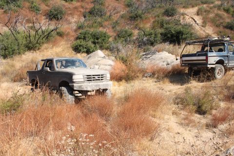 1992 Ford Bronco - Two trucks navigate a dry, grassy hillside trail.