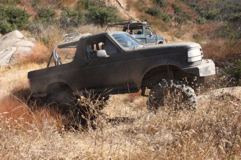 1992 Ford Bronco - Two SUVs navigate a dry, grassy, off-road trail with rocky terrain.