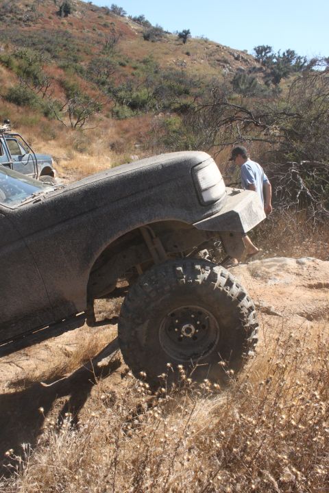 1992 Ford Bronco - A 1992 Ford Bronco navigates a rough, dry, hilly terrain with another vehicle visible in the background.