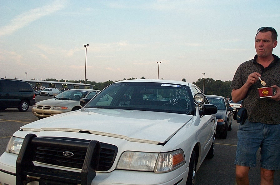 White Ford Crown Victoria ex-police car with push bumper and spotlight in an auction lot