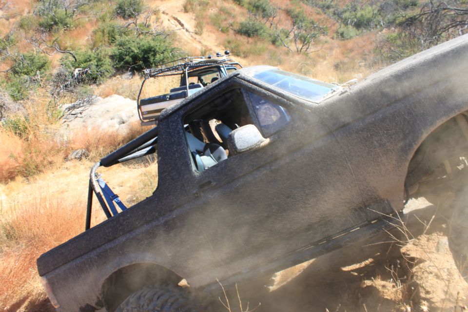 Two off-road vehicles climbing a dusty hill, one in foreground is dark and covered in dust