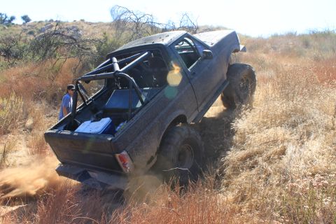 1992 Ford Bronco - A heavily modified off-road vehicle kicks up dust as it ascends a dry, grassy slope.