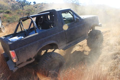 1992 Ford Bronco - A modified 1992 Ford Bronco navigates a dusty trail with a roll cage and oversized tires.