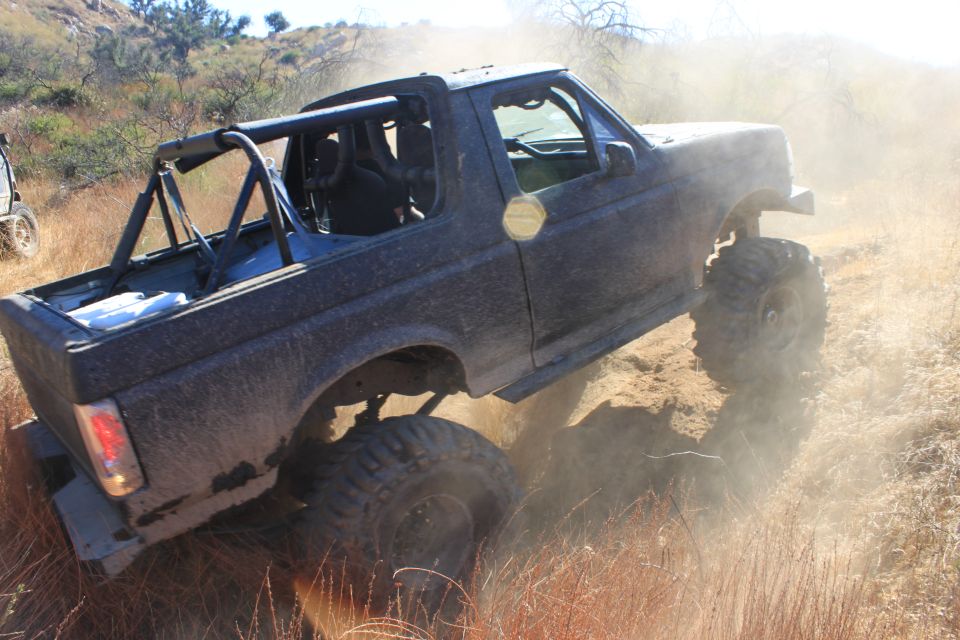 Dark 1992 Ford Bronco off-roading, kicking up dust, with a roll cage and large tires