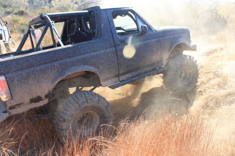 1992 Ford Bronco - This modified 1992 Ford Bronco navigates a challenging off-road trail, kicking up dust.