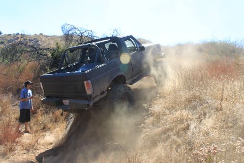 1992 Ford Bronco - A dark SUV kicks up dust as it navigates a steep, dry hillside.