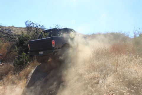 1992 Ford Bronco - This vehicle is navigating a challenging off-road terrain, kicking up a significant amount of dust.