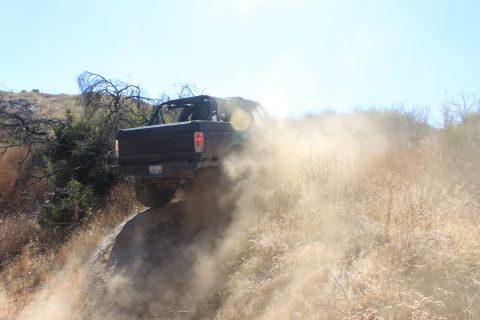 1992 Ford Bronco - A black SUV navigates a dusty, off-road trail, its rear visible as it kicks up a cloud of dirt.