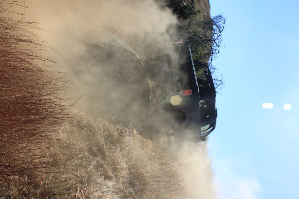 Black SUV driving on a dirt road, kicking up a large cloud of dust. Sunny day with blue sky