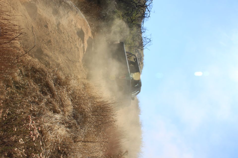 Dark off-road vehicle on a dusty dirt trail, viewed from the rear