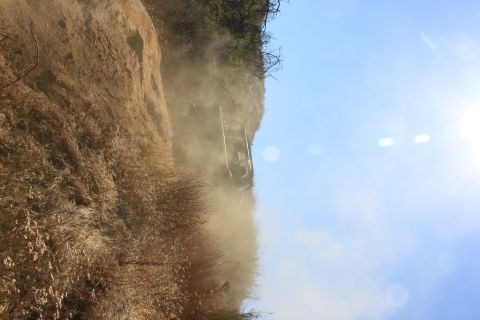 1992 Ford Bronco - An off-road vehicle navigates a steep, dusty trail, kicking up a cloud of dirt against a clear blue sky.