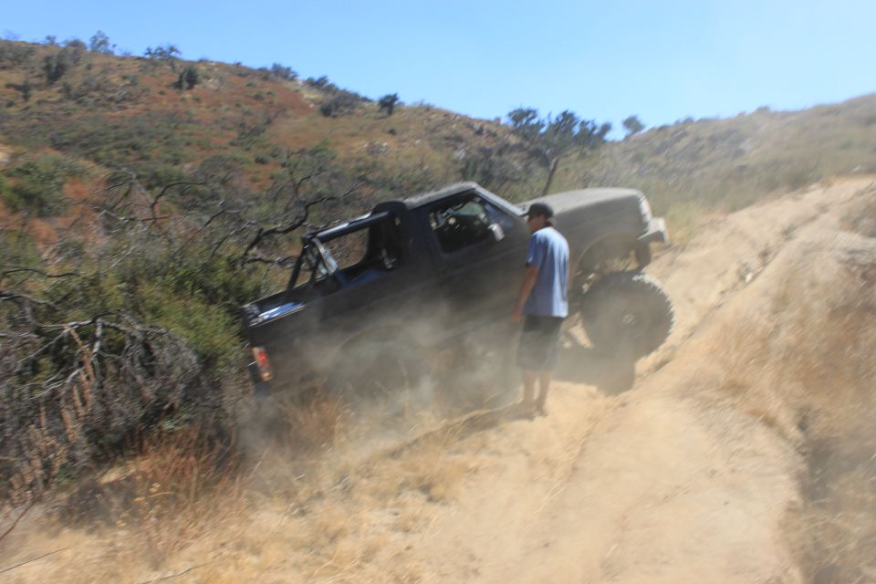 Black off-road truck on a dusty trail, driver's side visible, with a roll cage