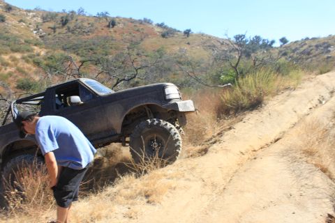 1992 Ford Bronco - A 1992 Ford Bronco navigates a steep, dusty trail with a person observing its progress.