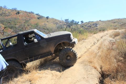 1992 Ford Bronco - A 1992 Ford Bronco navigates a challenging dirt path in a dry, hilly landscape.