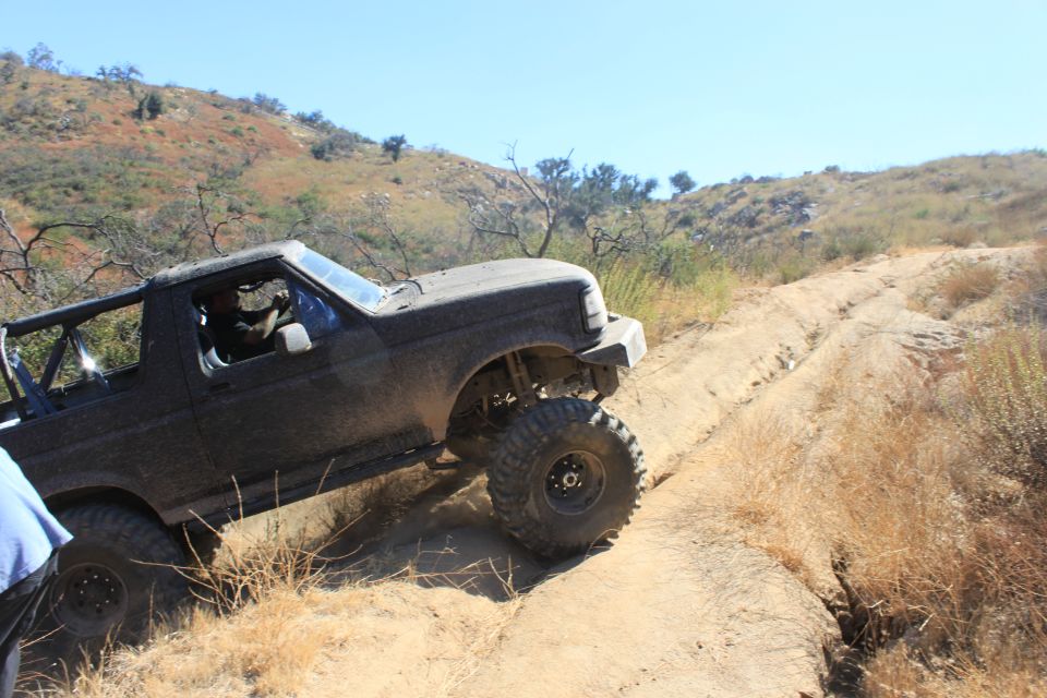 Black 1992 Ford Bronco with off-road modifications driving on a dirt trail