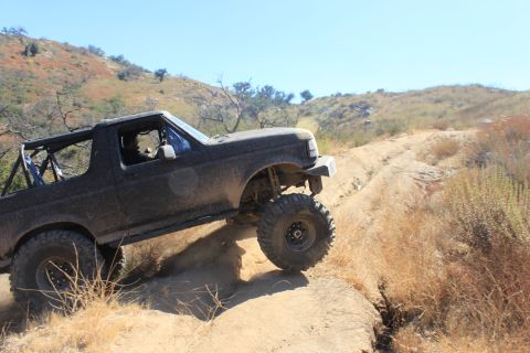 1992 Ford Bronco - This modified 1992 Ford Bronco navigates a challenging off-road trail under a clear blue sky.