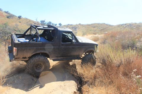 1992 Ford Bronco - This modified Ford Bronco is navigating a challenging off-road trail with steep inclines and rocky terrain.
