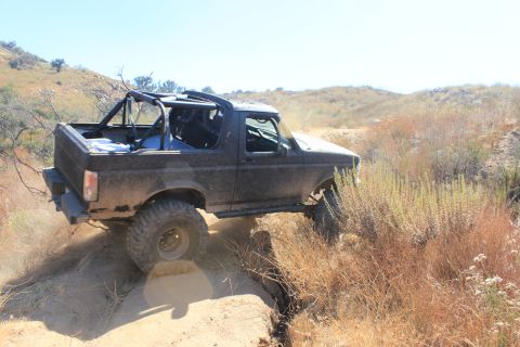 1992 Ford Bronco - A black 1992 Ford Bronco navigates a challenging dirt trail with its right front wheel lifted.