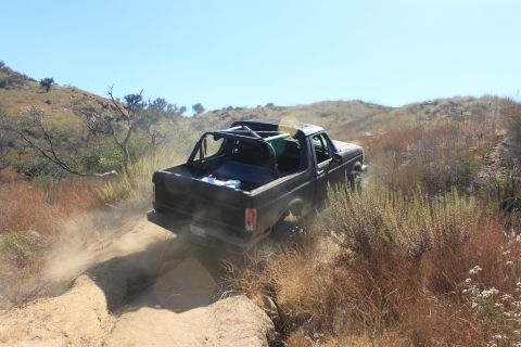 1992 Ford Bronco - 1992 Ford Bronco navigates a challenging dirt path in a dry, hilly landscape.