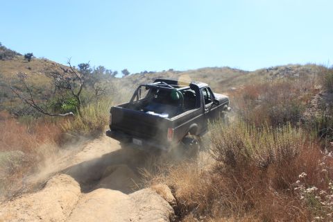 1992 Ford Bronco - A black Ford Bronco navigates a dusty, off-road trail under a clear blue sky.