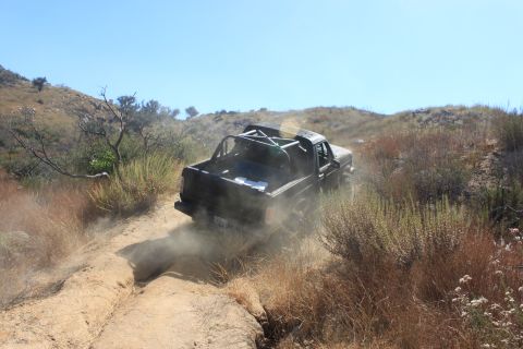 1992 Ford Bronco - A black pickup truck navigates a dusty trail through a dry, hilly landscape.