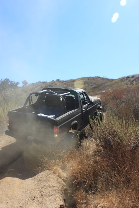 1992 Ford Bronco - 1992 Ford Bronco navigates a dusty trail in a dry, hilly landscape.