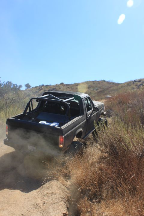 1992 Ford Bronco - A black Ford Bronco navigates a dusty off-road trail under a clear blue sky.