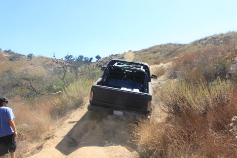 1992 Ford Bronco - A black pickup truck with an external roll cage navigates a dry, dusty trail under a clear blue sky.